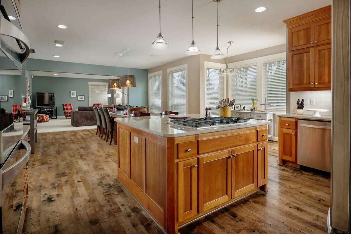 The image showcases a spacious, sunlit kitchen and dining area in a single-family home. The focal point is a large kitchen island with comfortable seating, surrounded by gleaming stainless steel appliances, an inviting dining area, and expansive windows that fill the space with natural light. The setting is perfect for group meals, lively cooking sessions, and memorable celebrations.