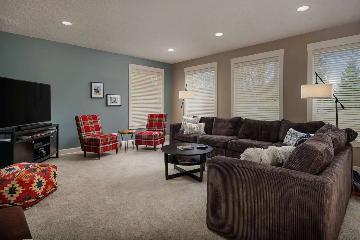 A spacious living room with plaid armchairs, a large sectional couch, a central black coffee table, and a stylish TV unit. The arrangement creates an inviting environment for group discussions, socializing, or unwinding after a work session. Natural light streams in, enhancing the comfort of the setting.
