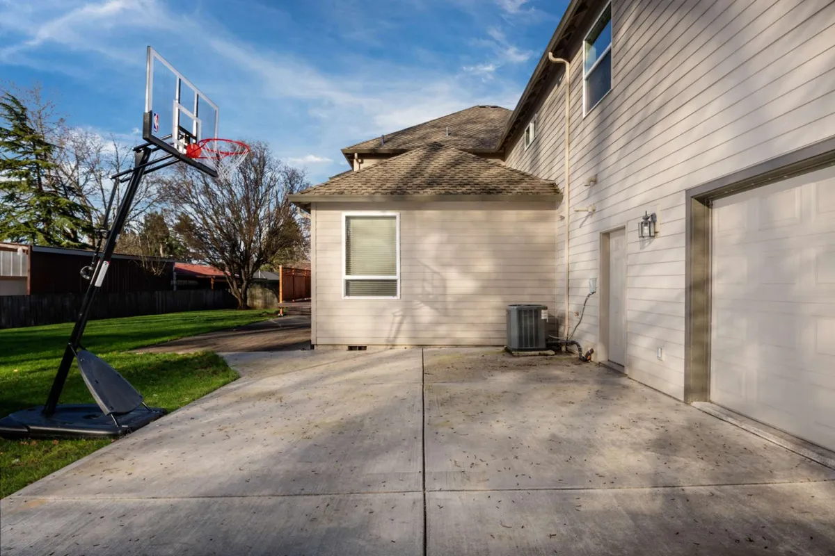 An exterior image focusing on the backyard basketball hoop, driveway, and the house's siding. The scene evokes an atmosphere of outdoor play, family gatherings, and fun in a safe and welcoming backyard setting.