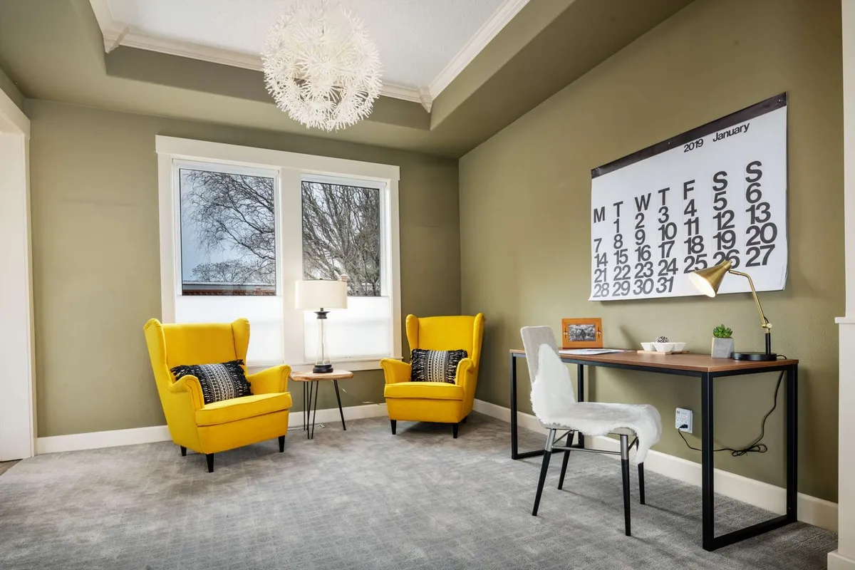 A bright and cheerful workspace furnished with yellow armchairs, a desk with a lamp, and a wall calendar. The arrangement is conducive to both independent work and collaborative projects, with plenty of natural light and a positive vibe.