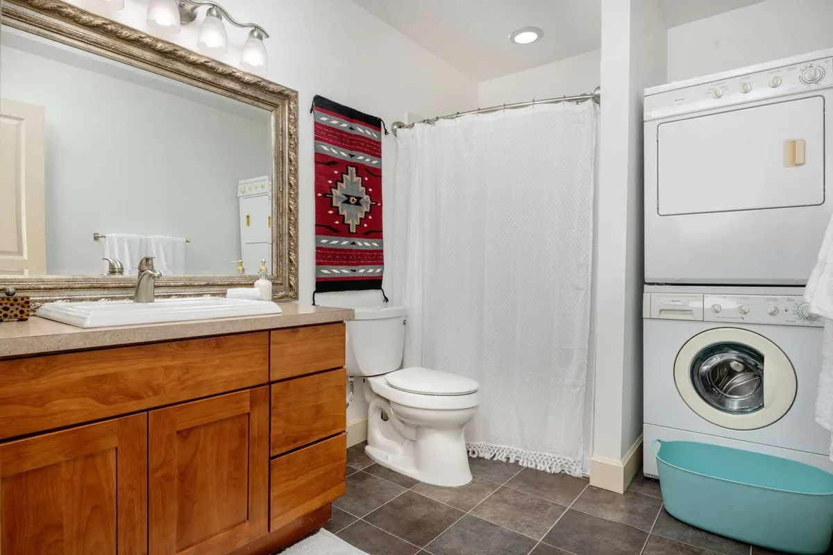 A practical laundry area featuring a vanity with a mirror, colorful wall hanging, and a washing machine. The space is inviting and functional, making everyday chores easy and accessible for guests.