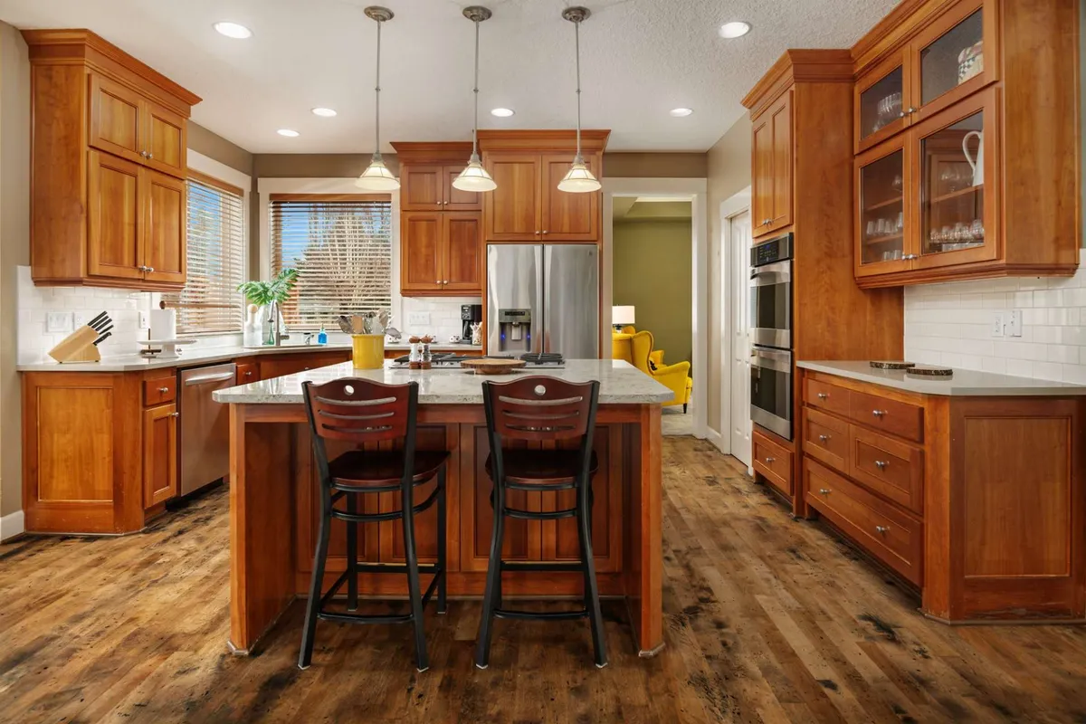 A spacious, modern kitchen with a central island surrounded by bar stools, wooden cabinetry, and gleaming stainless steel appliances. The setup invites both cooking and socializing, capturing the energy of group culinary activities.