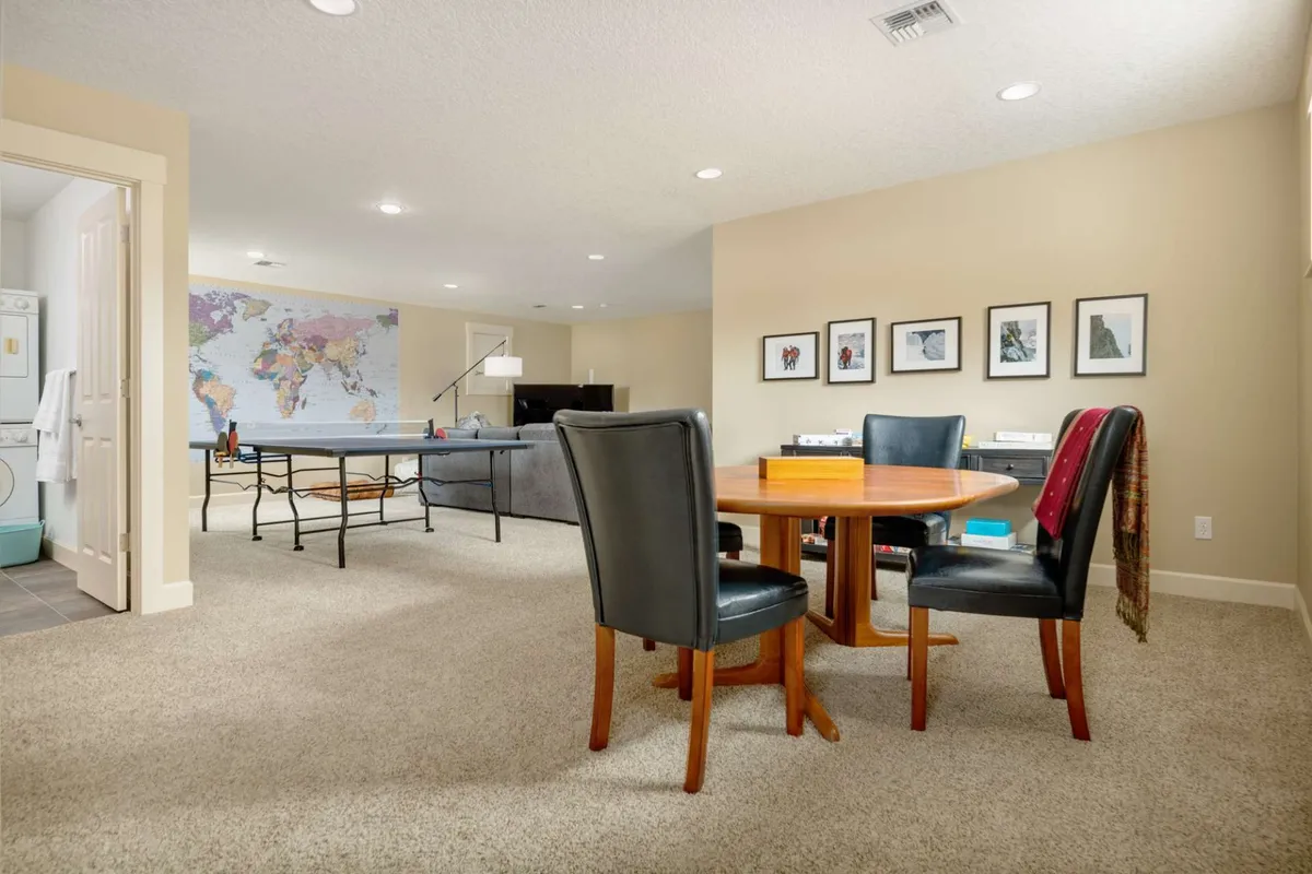 A round dining table surrounded by comfortable seating, set against a striking world map mural and accompanied by framed travel photographs. The scene suggests a welcoming space that celebrates global exploration and shared experiences.